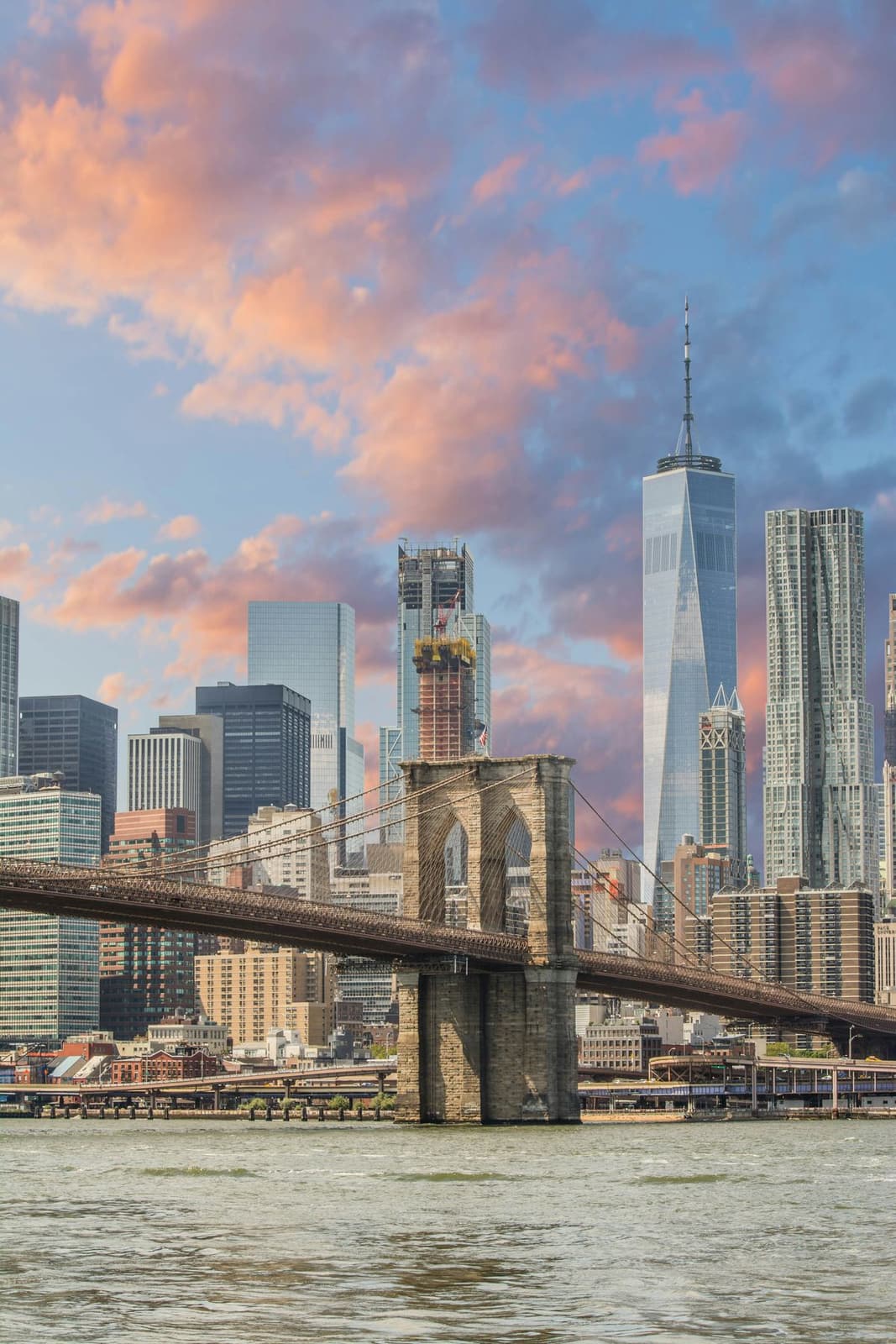 The Brooklyn Bridge and the Lower Manhattan skyline under a pink evening sky