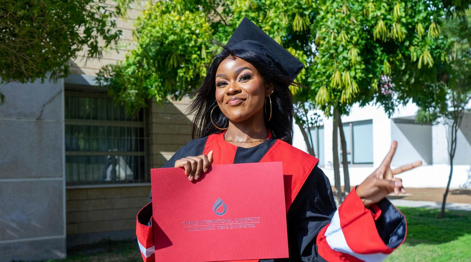 A smiling Black woman graduate in cap and gown holding her degree folder