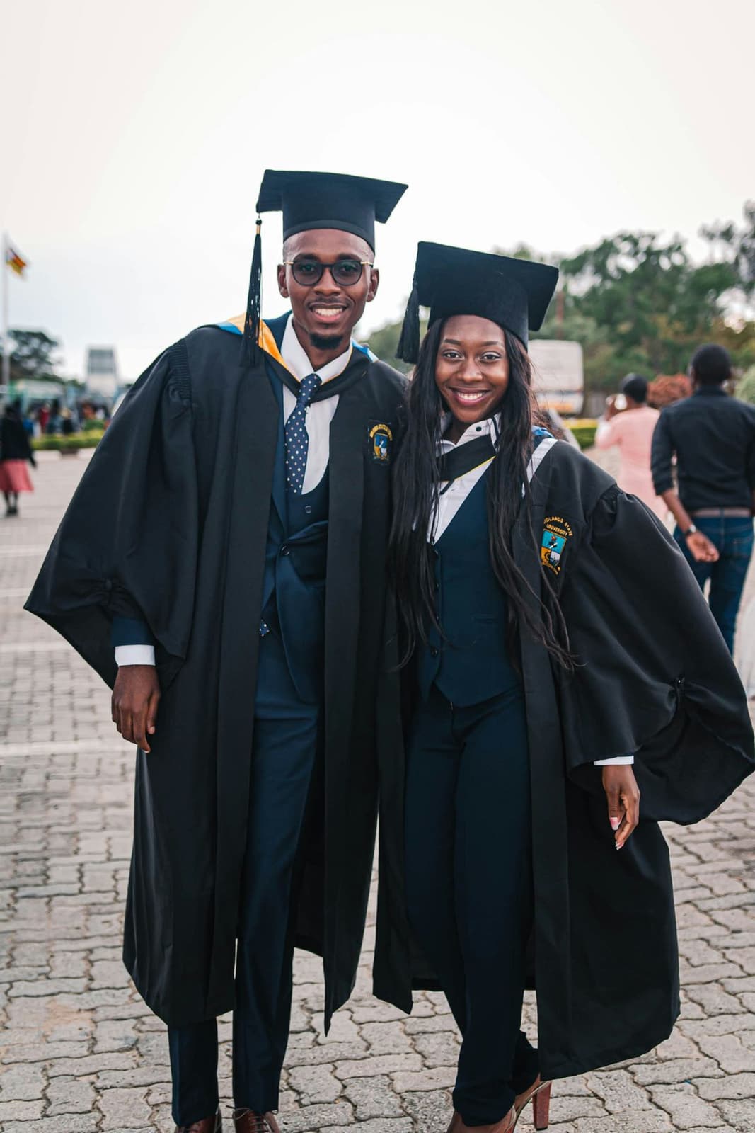 Two Black graduates in caps and gowns standing together on campus