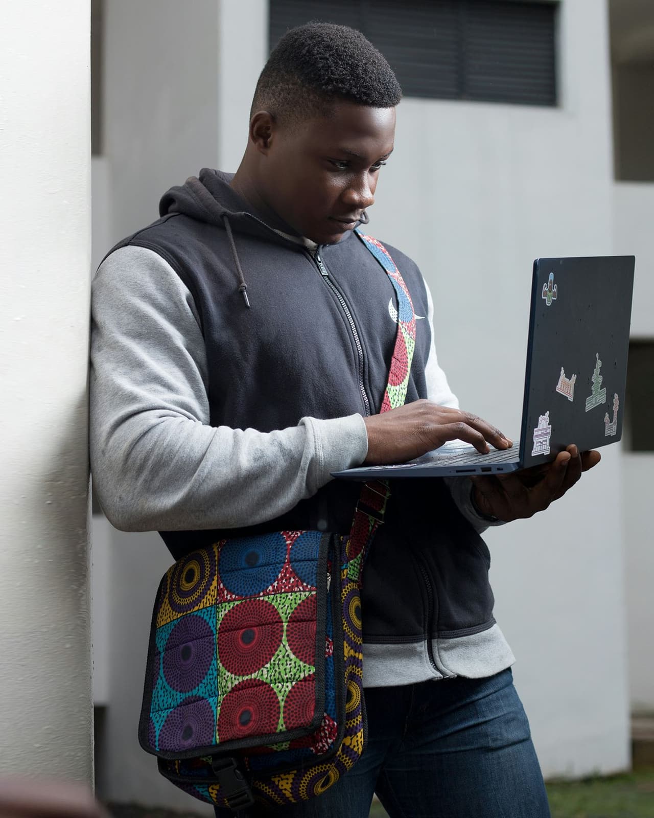 A Black man in a grey hoodie standing and working on a laptop in a modern office