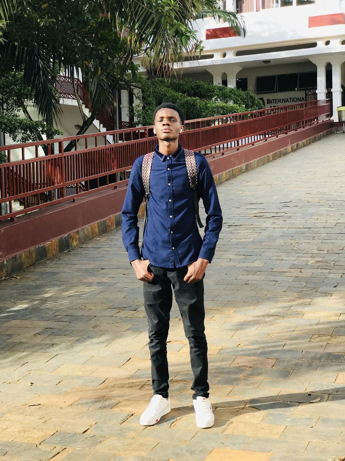 A young Black male student with a backpack standing on a university campus walkway