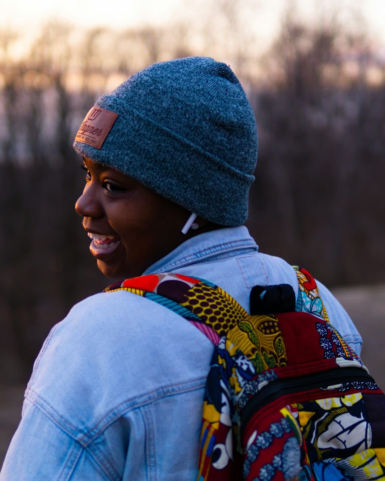 A young Black traveller in a knit cap and denim jacket with a colourful backpack