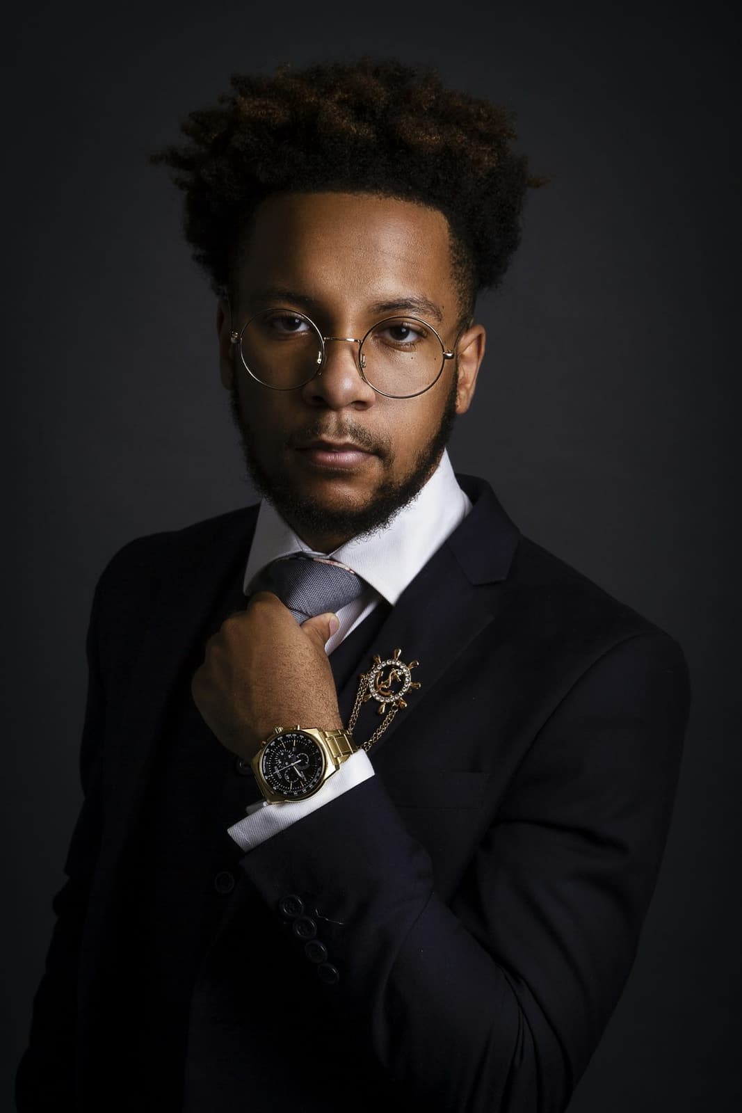 A Black man in a dark suit and glasses adjusting his watch