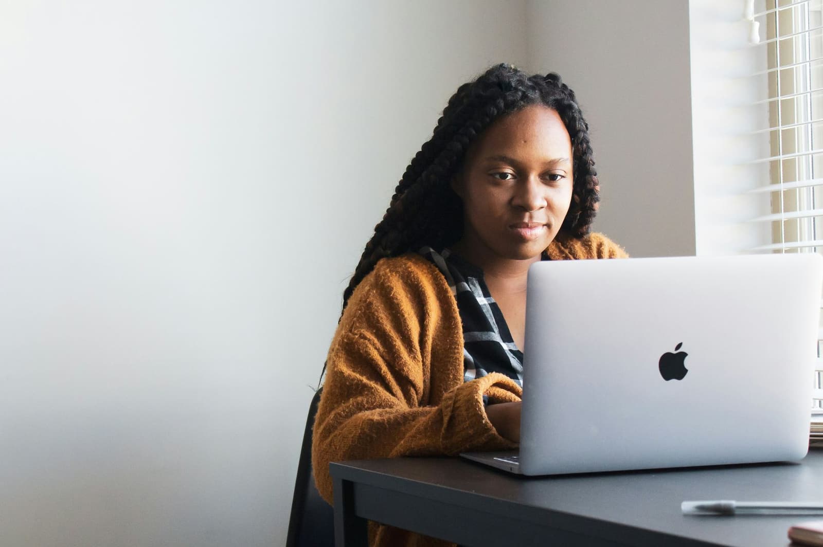 A Black woman with long braids working on a silver laptop at a desk
