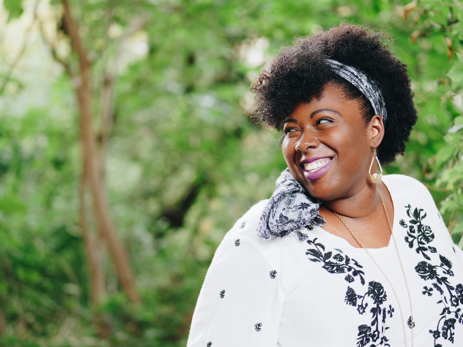 A smiling Black woman with natural hair and a headband outdoors