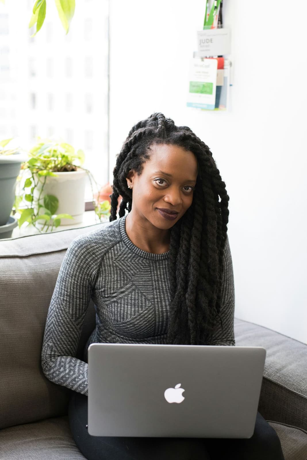 A Black woman sitting on a sofa searching on her laptop at home