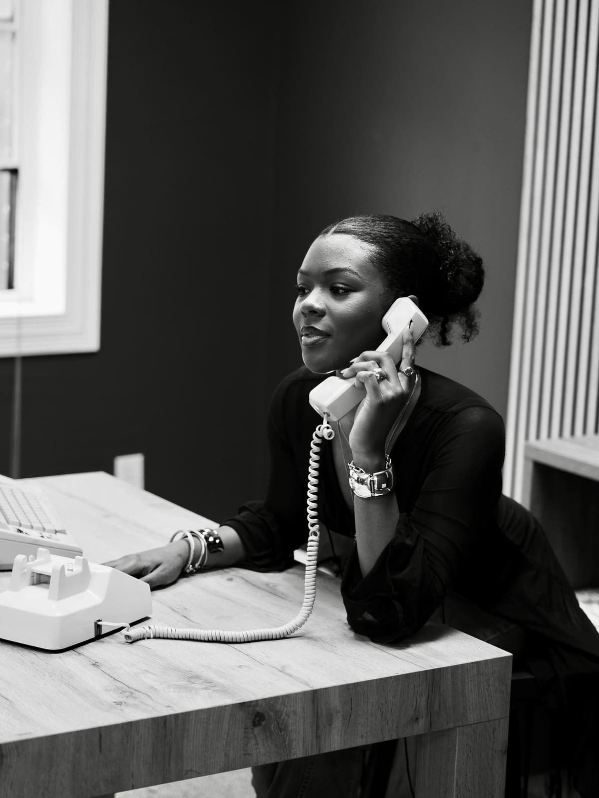 A Black woman smiling while talking on a telephone at a desk