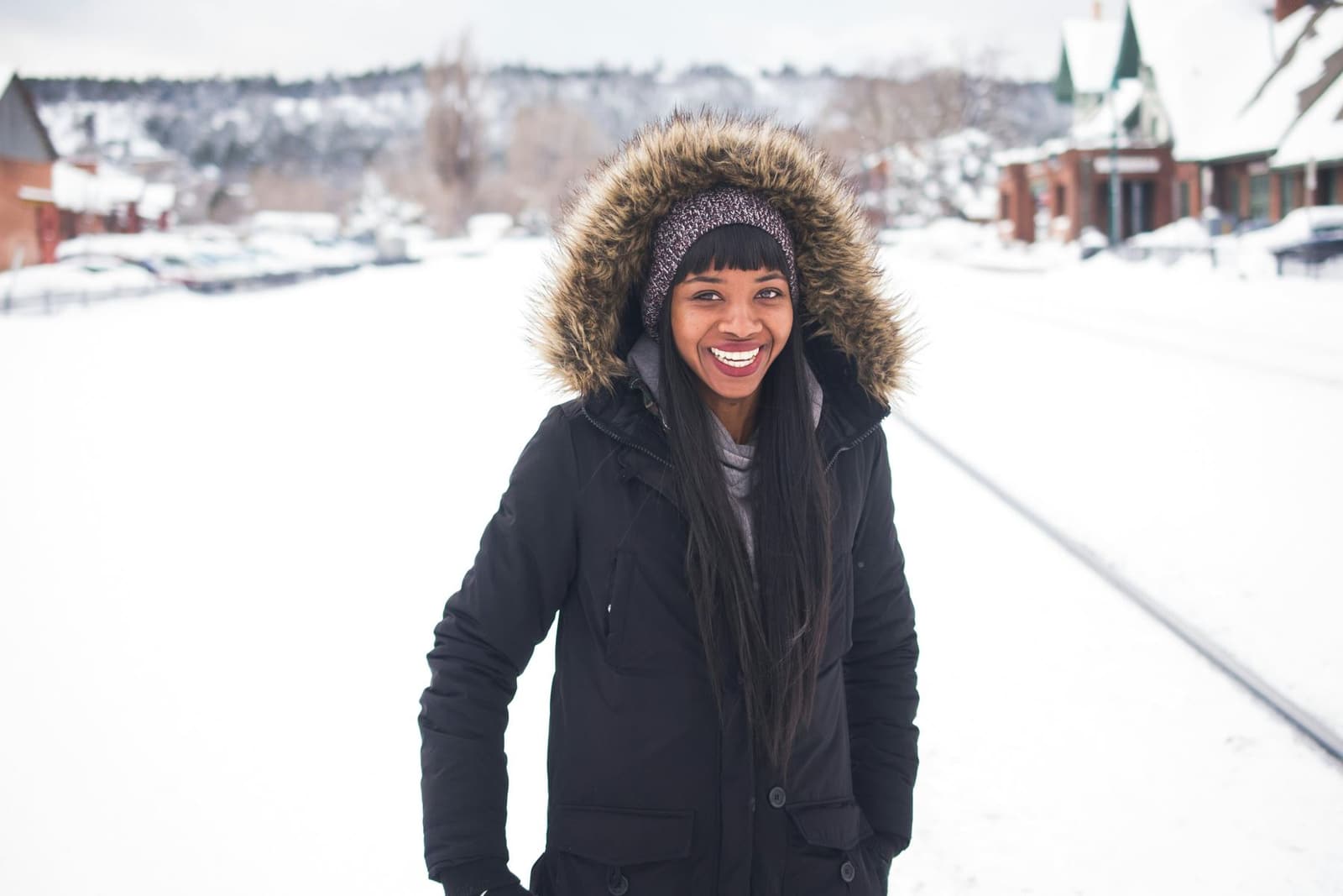 A smiling Black woman in a fur-hooded winter coat in a snowy street